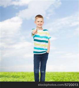 happiness, childhood, gesture, environment and people concept - smiling little boy his finger at you over natural background