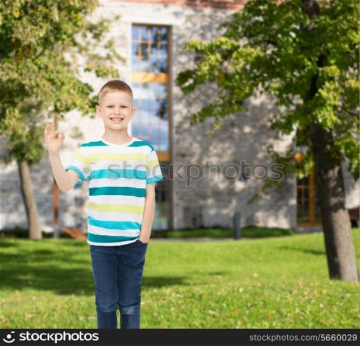 happiness, childhood, gesture, leisure and people concept - smiling little boy in casual clothes showing ok sign over campus background
