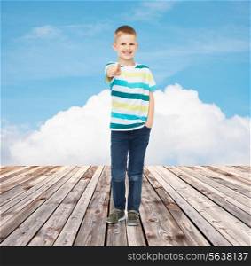 happiness, childhood, gesture, summer and people concept - smiling boy pointing finger at you over blue sky and wooden floor background