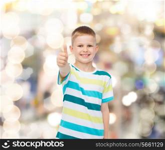 happiness, childhood, holidays, gesture and people concept - smiling little boy showing thumbs up over sparkling background