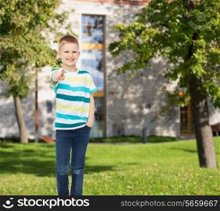happiness, childhood, leisure and people concept - smiling little boy in casual clothes pointing finger at you over campus background