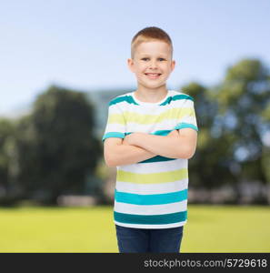 happiness, childhood, nature and people concept - smiling little boy in casual clothes with crossed arms over green park background