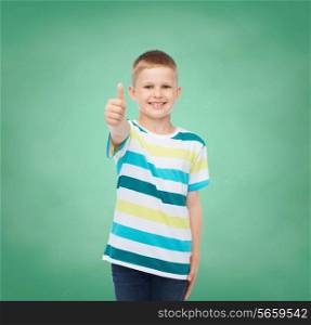happiness, childhood, school, education and people concept - smiling little boy showing thumbs up over green board background