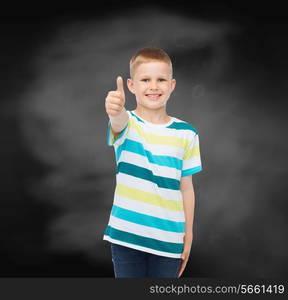 happiness, childhood, school, education and people concept - smiling little boy showing thumbs up over blackboard background