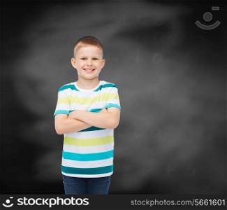 happiness, childhood, school, education and people concept - smiling little boy with crossed arms over blackboard background