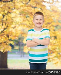 happiness, childhood, seasons and people concept - smiling little boy in casual clothes with crossed arms over autumn park background