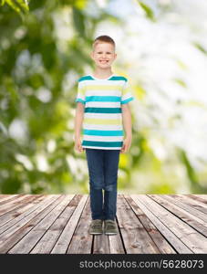 happiness, childhood, summer and people concept - smiling little boy in casual clothes over plants and wooden floor background