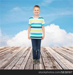 happiness, childhood, summer and people concept - smiling little boy in casual clothes over blue sky and wooden floor background