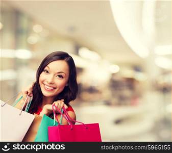 happiness, consumerism, sale and people concept - smiling young woman with shopping bags over mall background