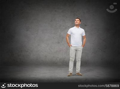 happiness, dreaming and people concept - smiling man with hands in pockets looking up over concrete background