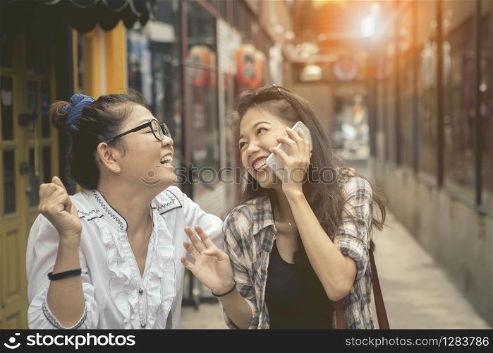 happiness emotion of asian two asian woman talking to smart phone and laughing in shopping street