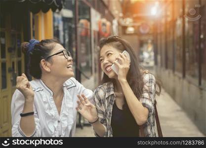 happiness emotion of asian two asian woman talking to smart phone and laughing in shopping street