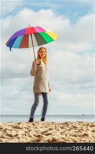 Happiness, enjoying autumn weather, feeling great concept. Woman holding colorful umbrella on cloudy blue sky. Happy woman holding umbrella