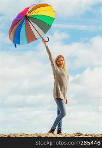 Happiness, enjoying autumn weather, feeling great concept. Woman holding colorful umbrella on cloudy blue sky. Happy woman holding umbrella