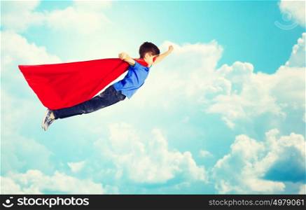 happiness, freedom, childhood, movement and people concept - boy in red superhero cape and mask flying in air over blue sky and clouds background. boy in red superhero cape and mask flying over sky