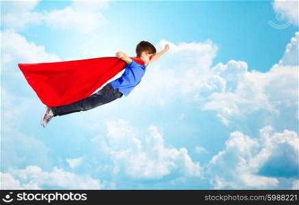 happiness, freedom, childhood, movement and people concept - boy in red superhero cape and mask flying in air over blue sky and clouds background