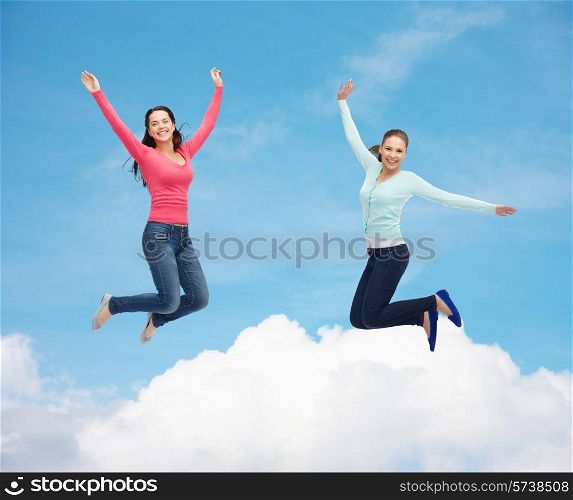 happiness, freedom, friendship, movement and people concept - smiling young women jumping in air over blue sky with white cloud background