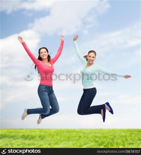 happiness, freedom, friendship, movement, summer and people concept - smiling young women jumping in air over natural background