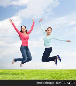 happiness, freedom, friendship, movement, summer and people concept - smiling young women jumping in air over natural background