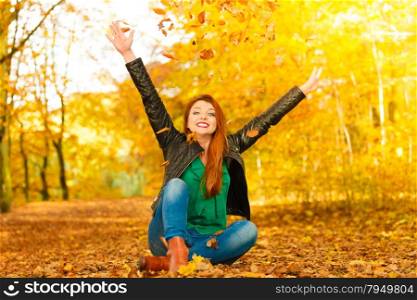 Happiness freedom leisure concept. Redhair woman relaxing in autumn park throwing leaves up in the air. Beautiful girl in orange forest foliage outdoor.