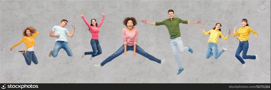 happiness, freedom, motion and people concept - smiling young international friends jumping in air over gray concrete background. happy people or friends jumping in air over gray