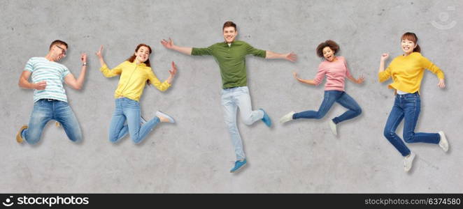 happiness, freedom, motion and people concept - smiling young international friends jumping in air over gray concrete background. happy people or friends jumping in air over gray