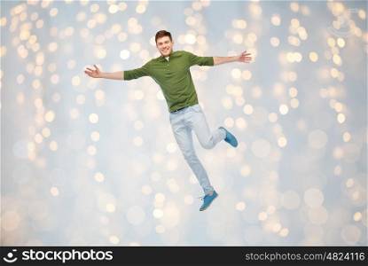 happiness, freedom, motion and people concept - smiling young man jumping in air over holidays lights background