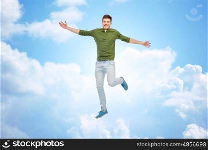 happiness, freedom, motion and people concept - smiling young man jumping in air over blue sky and clouds background