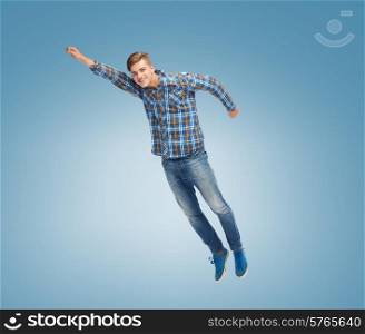 happiness, freedom, movement and people concept - smiling young man flying in air over blue background