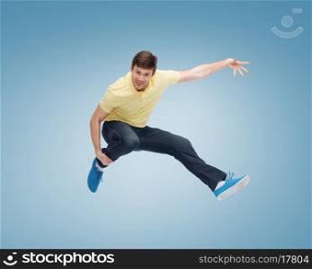 happiness, freedom, movement and people concept - smiling young man jumping in air over blue background