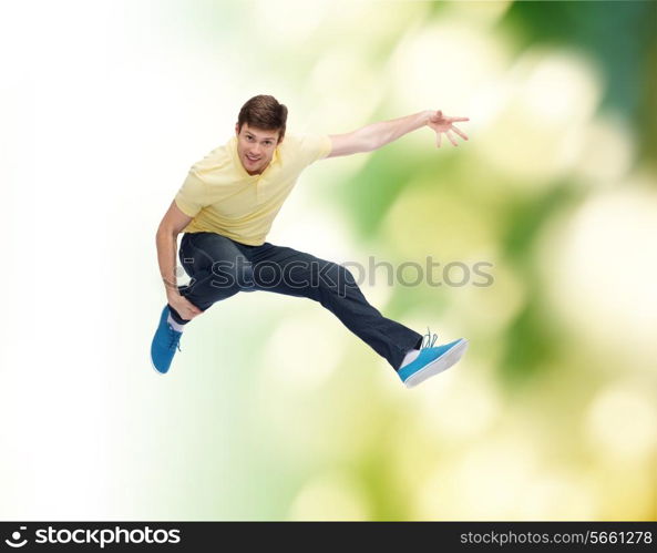 happiness, freedom, movement, ecology and people concept - smiling young man jumping in air over green background