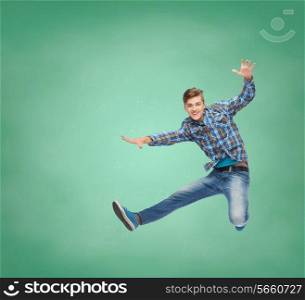 happiness, freedom, movement, education and people concept - smiling young man jumping in air over over green board background