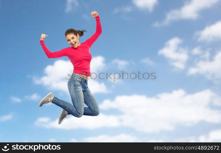 happiness, freedom, power, motion and people concept - smiling young woman jumping in air with raised fists over blue sky and clouds background