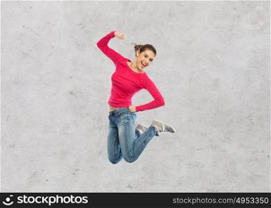 happiness, freedom, power, motion and people concept - smiling young woman jumping in air with raised fist over gray concrete wall background. smiling young woman jumping in air