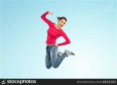 happiness, freedom, power, motion and people concept - smiling young woman jumping in air with raised fist over blue background. smiling young woman jumping in air