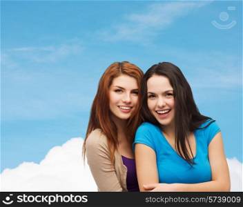 happiness, friendship and people concept - smiling teenage girls hugging over blue sky and cloud background
