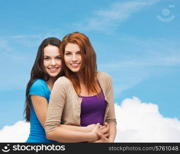 happiness, friendship and people concept - smiling teenage girls hugging over blue sky and cloud background