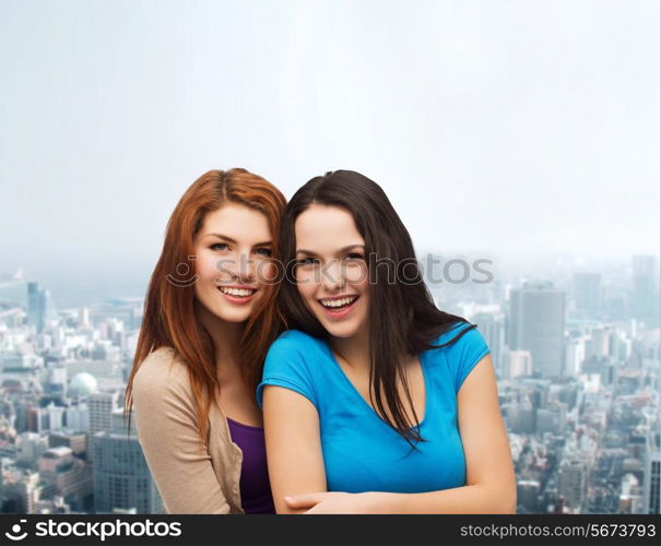 happiness, friendship and people concept - smiling teenage girls hugging over city background