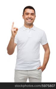 happiness, gesture and people concept - smiling man pointing finger up