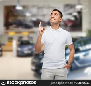 happiness, gesture and people concept - smiling man pointing finger up over auto show background