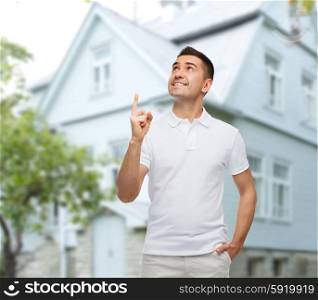 happiness, gesture and people concept - smiling man pointing finger up over house background