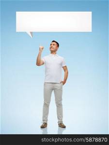 happiness, gesture and people concept - smiling man pointing finger up to white blank text bubble over blue background