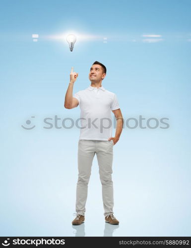 happiness, gesture and people concept - smiling man pointing finger up to lighting bulb over blue background