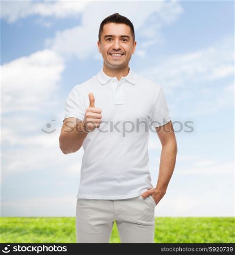 happiness, gesture and people concept - smiling man showing thumbs up over blue sky and grass background