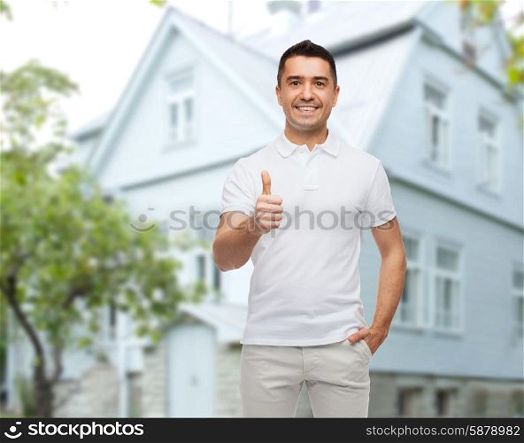 happiness, gesture and people concept - smiling man showing thumbs up over house background