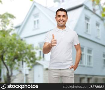 happiness, gesture and people concept - smiling man showing thumbs up over house background