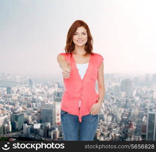 happiness, gesture, city life and people concept - smiling teenage girl in casual clothes showing thumbs up over city background