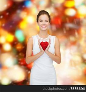 happiness, health, charity and love concept - smiling woman in white dress with red heart over party lights background