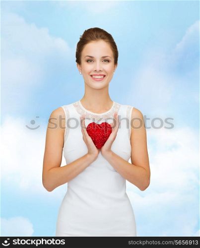 happiness, health, charity and love concept - smiling woman in white dress with red heart over blue cloudy sky background