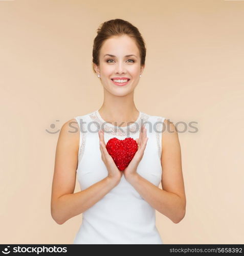 happiness, health, charity and love concept - smiling woman in white dress with red heart over beige background